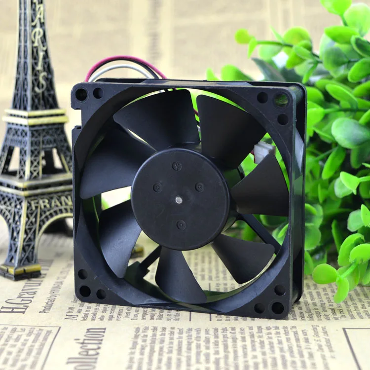 Un ventilador negro se sienta en una mesa al lado de una planta verde