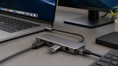 Detalle de un portátil conectado a un hub USB-C con HDMI, red y periféricos de oficina.