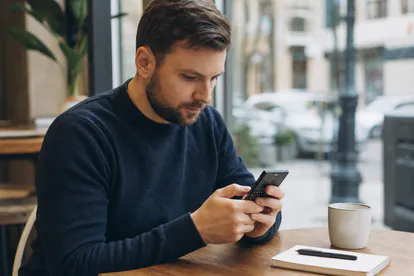 Persona escribe un mensaje largo con los pulgares sobre un teclado móvil físico